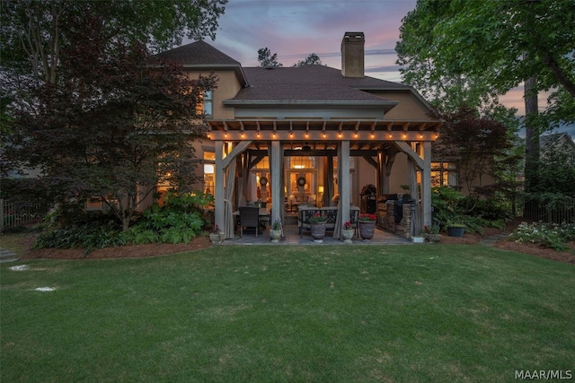 back house at dusk featuring a pergola, a patio area, and a lawn