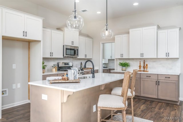 kitchen with light countertops, visible vents, decorative backsplash, appliances with stainless steel finishes, and an island with sink