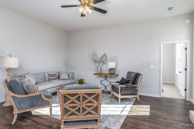 living room featuring a ceiling fan, visible vents, baseboards, and wood finished floors