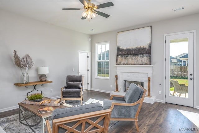 living room with a fireplace with raised hearth, wood finished floors, visible vents, and baseboards