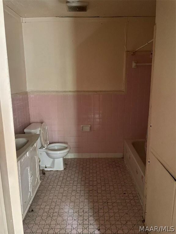 bathroom with vanity, toilet, tile walls, and a washtub