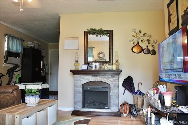 living room featuring wood-type flooring, a textured ceiling, a stone fireplace, and crown molding