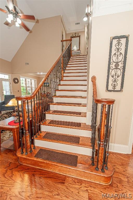 staircase featuring wood-type flooring, high vaulted ceiling, and ceiling fan