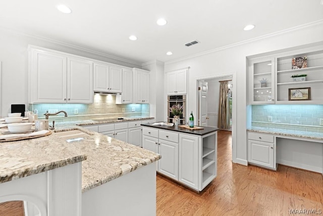 kitchen with a center island, backsplash, sink, black electric cooktop, and white cabinetry