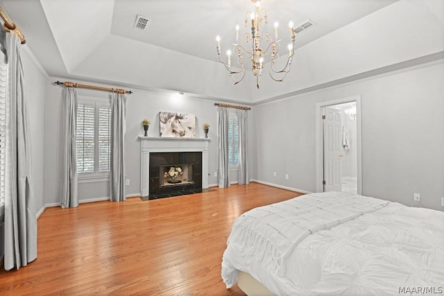 bedroom featuring hardwood / wood-style floors, a raised ceiling, a tile fireplace, and an inviting chandelier