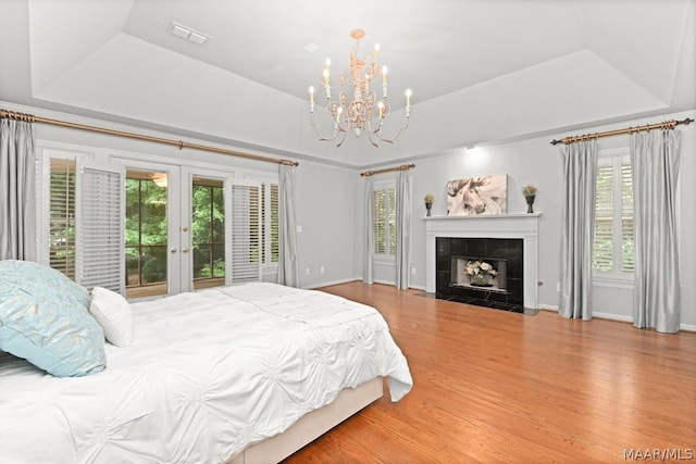 bedroom featuring a raised ceiling, a tiled fireplace, multiple windows, and access to outside