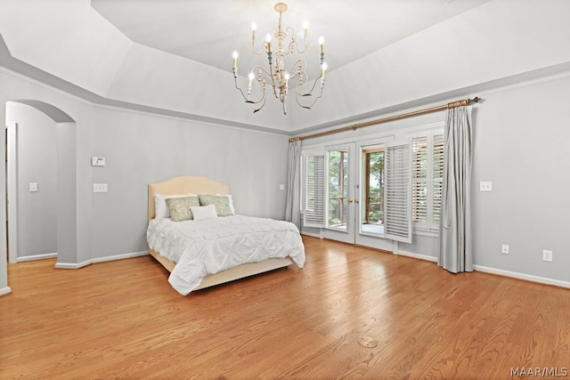 bedroom with a raised ceiling, access to exterior, light hardwood / wood-style floors, and an inviting chandelier