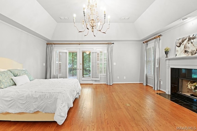 bedroom featuring a raised ceiling, access to outside, wood-type flooring, and a tile fireplace