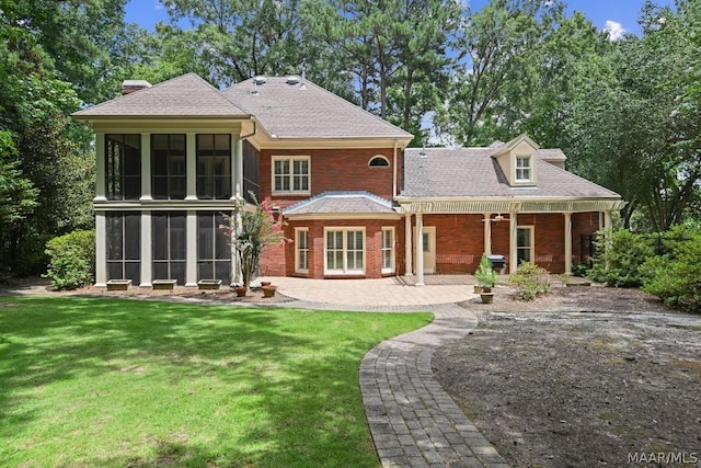 back of property with a sunroom, a patio area, and a lawn