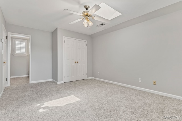 unfurnished bedroom featuring a skylight, ceiling fan, a closet, and light carpet