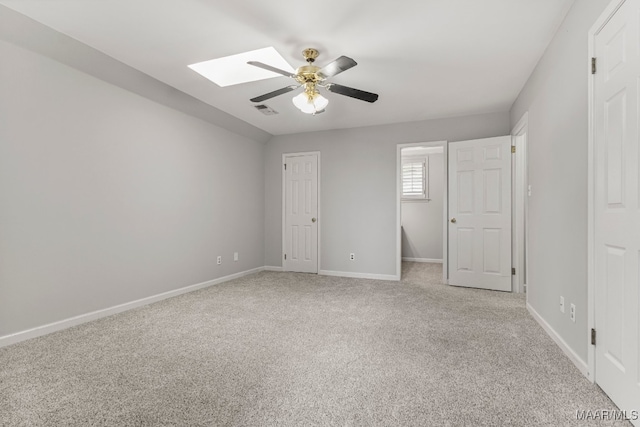 unfurnished bedroom with light carpet, a skylight, and ceiling fan