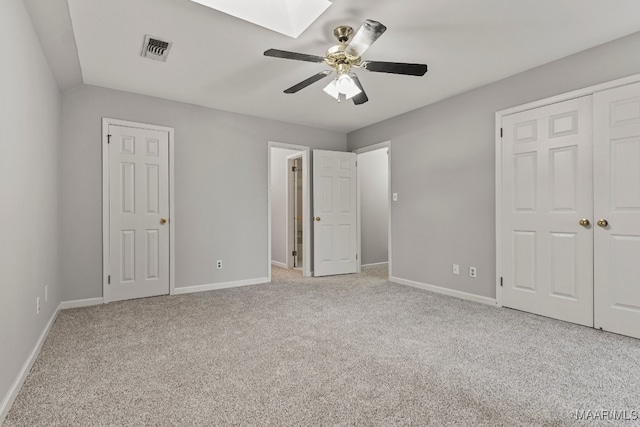 unfurnished bedroom with light carpet, a skylight, and ceiling fan