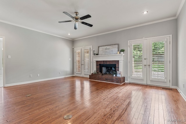 unfurnished living room featuring wood-type flooring, french doors, crown molding, a brick fireplace, and ceiling fan