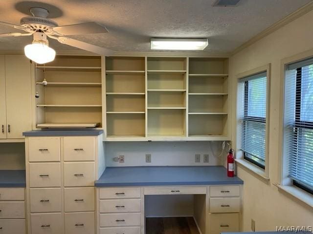 unfurnished office featuring ceiling fan, crown molding, built in desk, and a textured ceiling