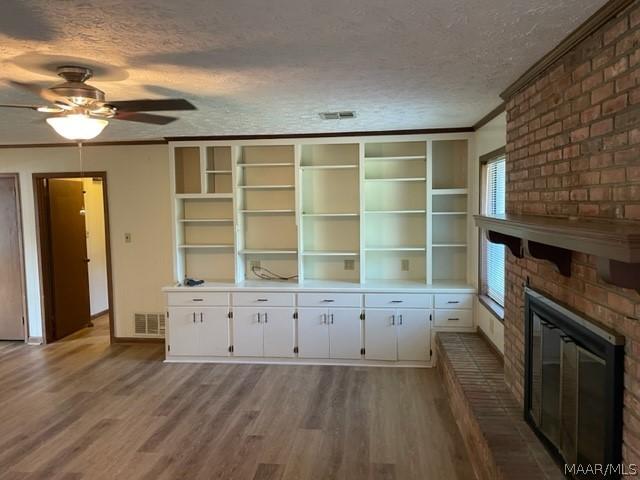 unfurnished living room featuring crown molding, a fireplace, wood-type flooring, and a textured ceiling