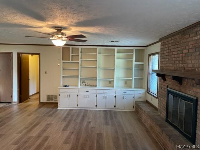 unfurnished living room with crown molding, wood-type flooring, a textured ceiling, and a brick fireplace