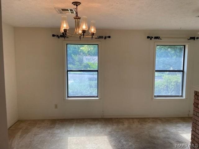 spare room featuring carpet, a textured ceiling, and a notable chandelier