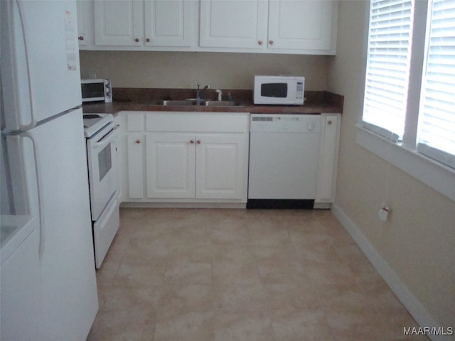 kitchen featuring dark countertops, a sink, baseboards, and white appliances