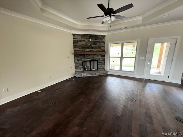 unfurnished living room featuring crown molding, a tray ceiling, a stone fireplace, and dark hardwood / wood-style flooring