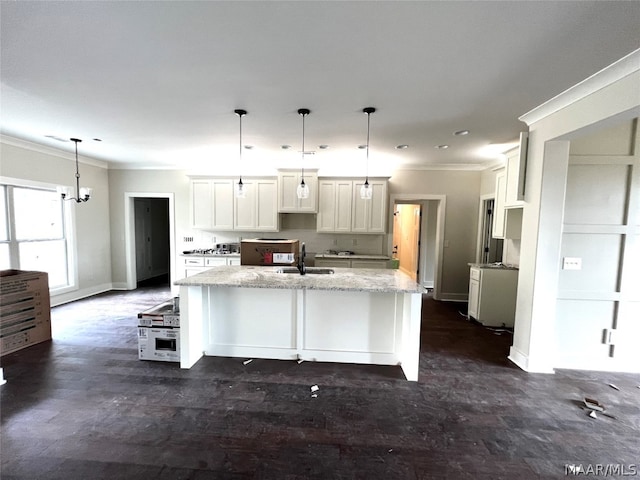 kitchen with sink, light stone countertops, hanging light fixtures, an island with sink, and white cabinetry