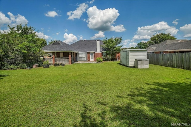 back of house with a fenced backyard, a storage shed, brick siding, an outdoor structure, and a yard