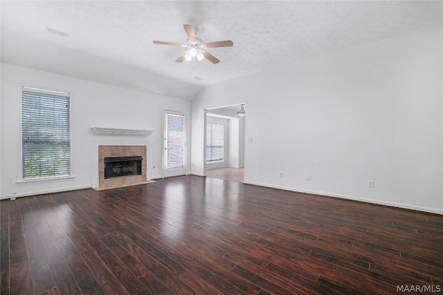 unfurnished living room featuring dark wood-type flooring, vaulted ceiling, ceiling fan, a textured ceiling, and a tiled fireplace