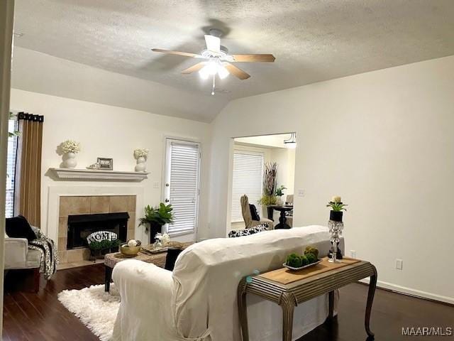 living area featuring ceiling fan, a textured ceiling, a tile fireplace, dark wood-style flooring, and vaulted ceiling