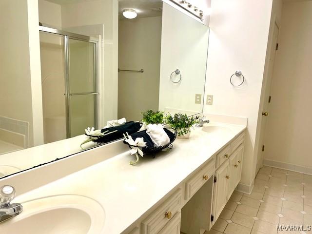 full bath with double vanity, a sink, a shower stall, tile patterned flooring, and baseboards