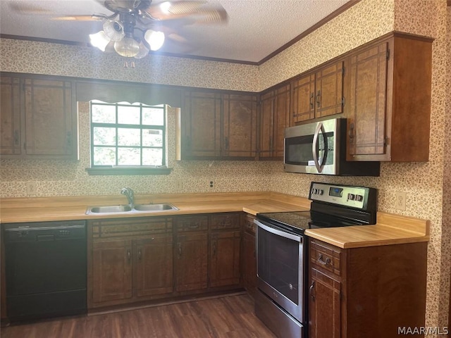 kitchen with stainless steel appliances, a sink, light countertops, wallpapered walls, and crown molding