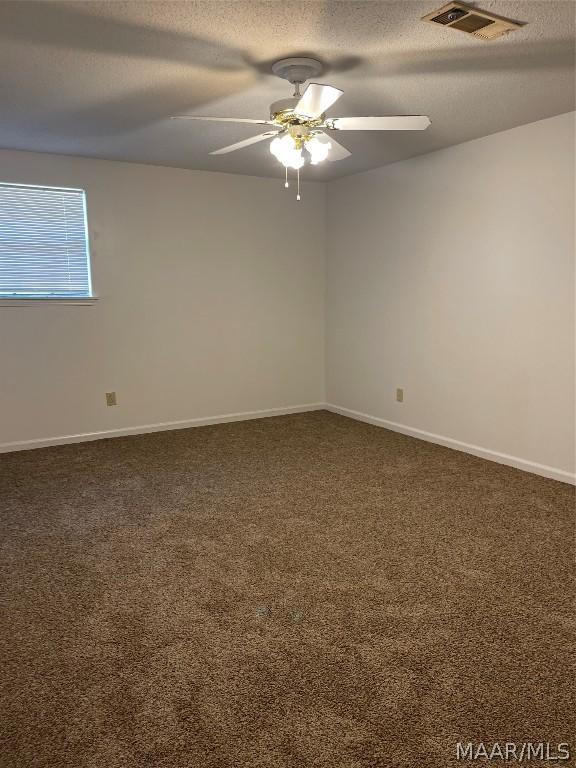 carpeted empty room featuring baseboards, ceiling fan, visible vents, and a textured ceiling