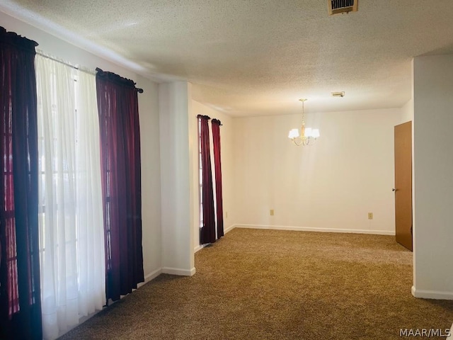 carpeted spare room featuring plenty of natural light, visible vents, a chandelier, and a textured ceiling