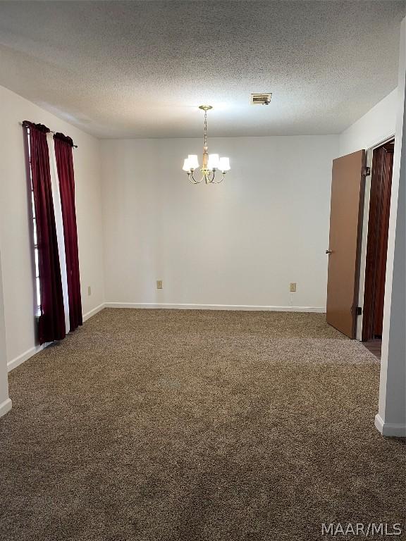 empty room with a notable chandelier, dark colored carpet, and a textured ceiling