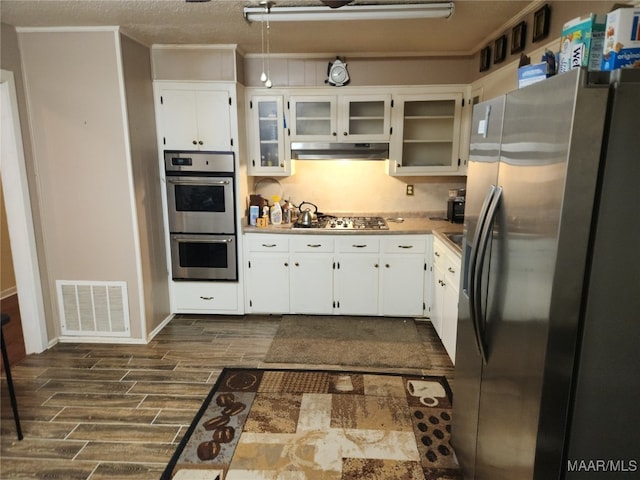 kitchen with dark wood-type flooring, appliances with stainless steel finishes, a textured ceiling, and white cabinets