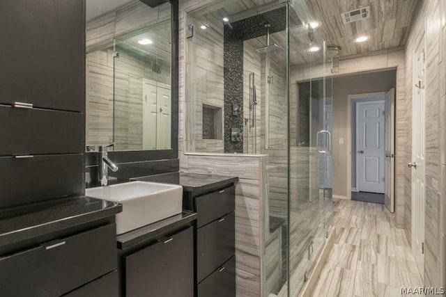 bathroom with a stall shower, vanity, visible vents, and tile walls