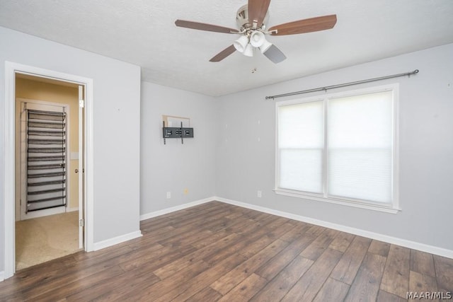 empty room with a textured ceiling, wood finished floors, a ceiling fan, and baseboards