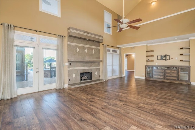 unfurnished living room featuring french doors, a tiled fireplace, a ceiling fan, wood finished floors, and baseboards