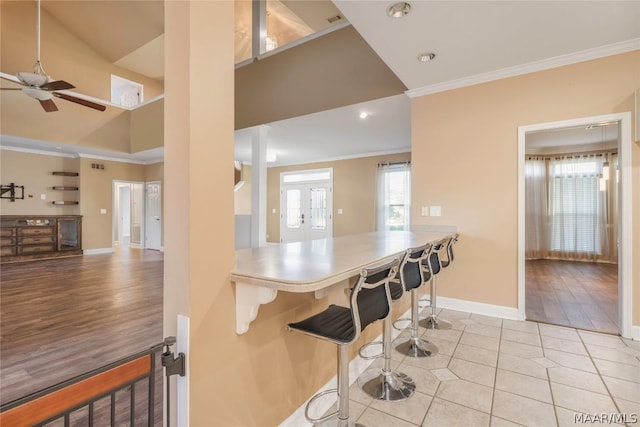 kitchen with light tile patterned floors, a breakfast bar, baseboards, french doors, and ornamental molding