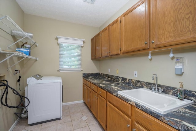 laundry area featuring light tile patterned floors, cabinet space, a sink, a textured ceiling, and baseboards