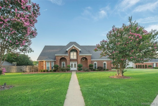 traditional home featuring brick siding, fence, a front lawn, and french doors