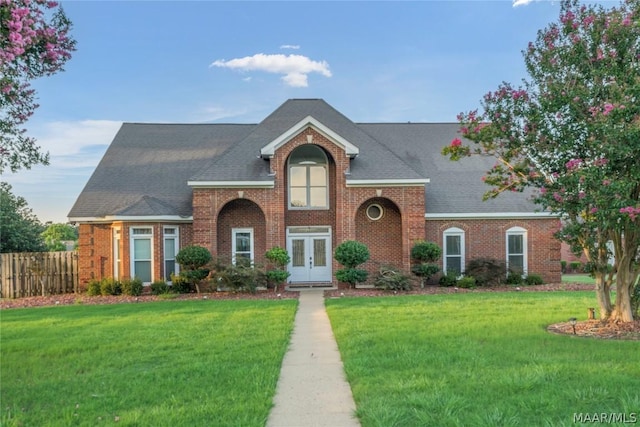 view of front of property featuring french doors, brick siding, and a front lawn