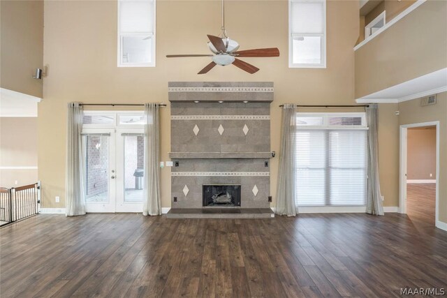 unfurnished living room with dark hardwood / wood-style floors, a towering ceiling, a tiled fireplace, and ceiling fan