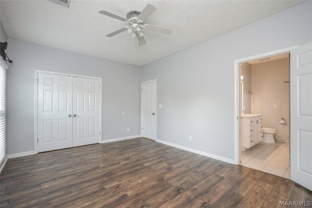 unfurnished bedroom featuring ceiling fan, wood finished floors, baseboards, a closet, and ensuite bath