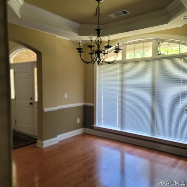 unfurnished dining area featuring hardwood / wood-style flooring, a tray ceiling, ornamental molding, and an inviting chandelier