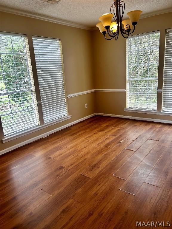 unfurnished room featuring wood-type flooring, a textured ceiling, an inviting chandelier, and a wealth of natural light