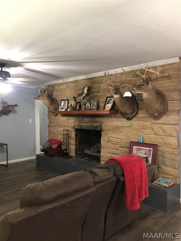 living room featuring a stone fireplace, dark wood-type flooring, ceiling fan, and crown molding