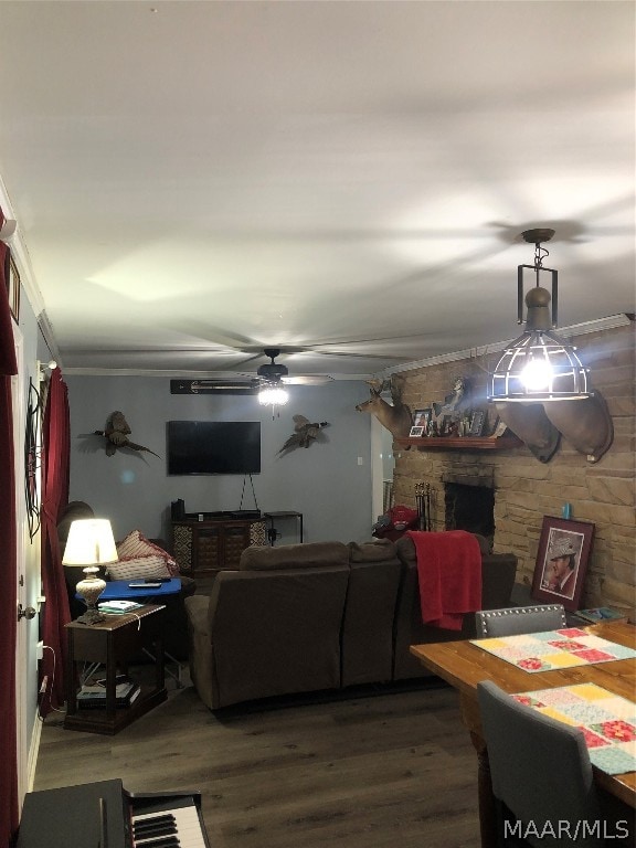 dining area with a stone fireplace, hardwood / wood-style flooring, ornamental molding, and ceiling fan