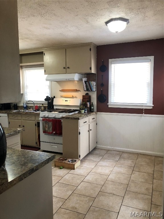 kitchen featuring a textured ceiling, white gas stove, a wealth of natural light, and light tile patterned flooring