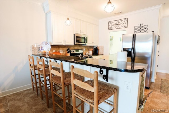 kitchen featuring a breakfast bar area, white cabinetry, stainless steel appliances, decorative light fixtures, and kitchen peninsula