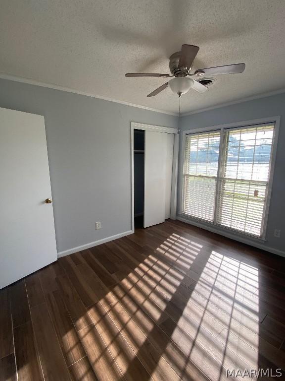 unfurnished bedroom with ceiling fan, dark hardwood / wood-style floors, crown molding, a textured ceiling, and a closet