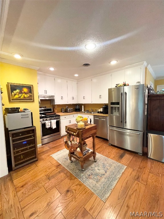 kitchen with a textured ceiling, white cabinets, stainless steel appliances, and light hardwood / wood-style floors